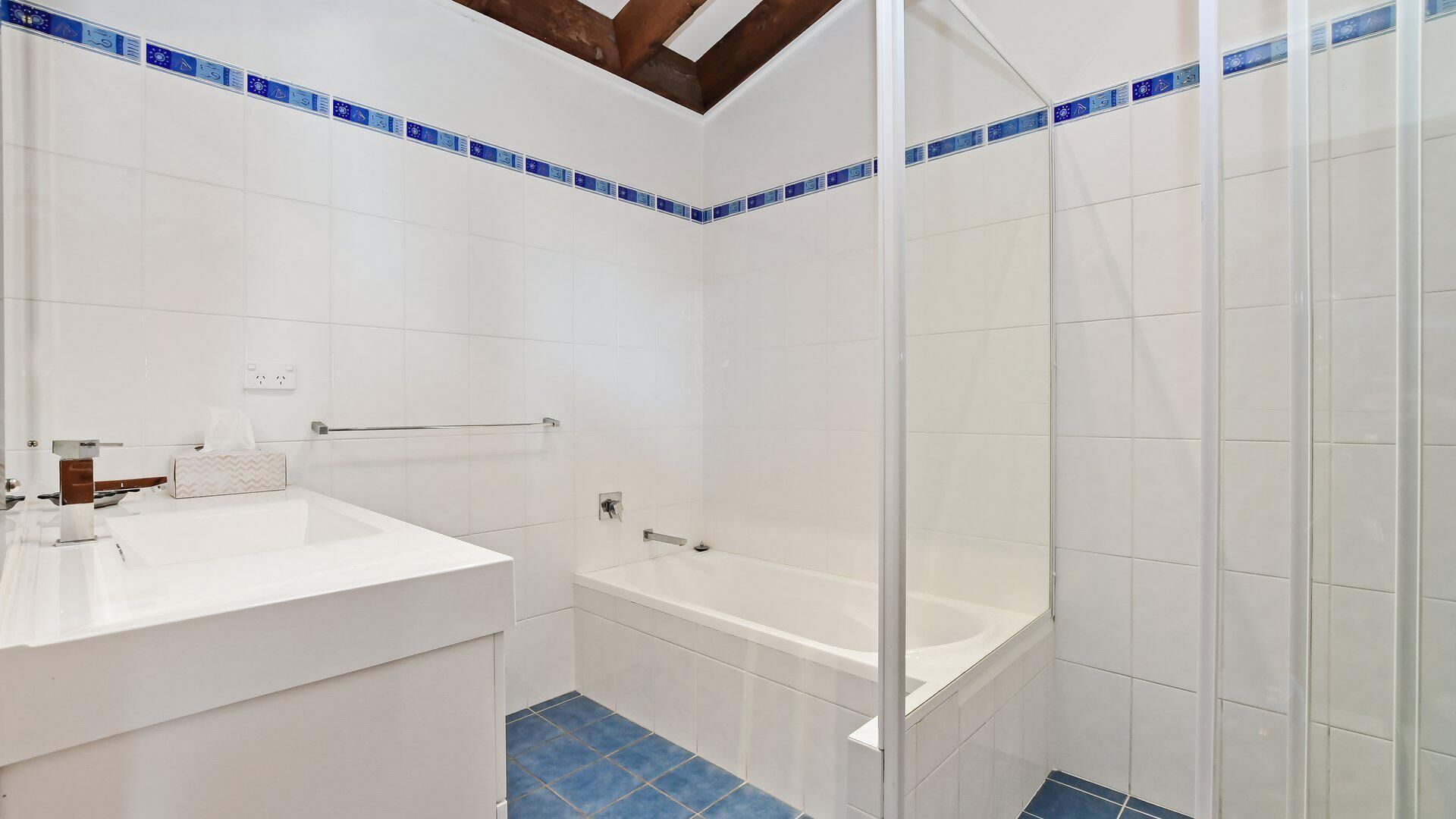 A bathroom with white tiles, a bathtub, a shower enclosure, and a sink area.