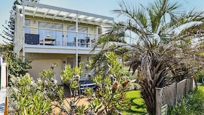 Een modern herenhuis met twee verdiepingen en een balkon, omgeven door weelderige beplanting en een palmboom.