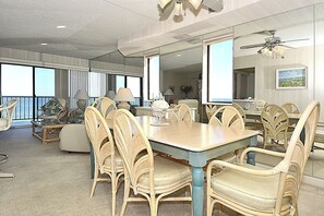 A dining area with a large table and wicker chairs, a ceiling fan, and large windows with a view. - LINENS & DAILY ACTIVITIES INCLUDED**!!! OCEAN VIEWS! THE CAPRI - 3BR/2BA - Direct OF Condo! (Ocean City)
