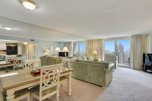 Habitación de hotel con comedor, sala de estar con sofá y televisor, y balcón con vistas.