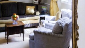 A room with a sofa, armchair, and a small table with a fruit bowl. There is a painting on the wall and a vase with flowers. - MORNING CHECK-IN IS GIVEN WHEN POSSIBLE -3BEDROOMS/2BATHS KNIGHTSBRIDGE (LONDON)