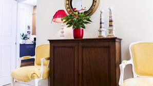 A room with a wooden cabinet, a red vase with flowers, a mirror, and two chairs. - MORNING CHECK-IN IS GIVEN WHEN POSSIBLE -3BEDROOMS/2BATHS KNIGHTSBRIDGE (LONDON)