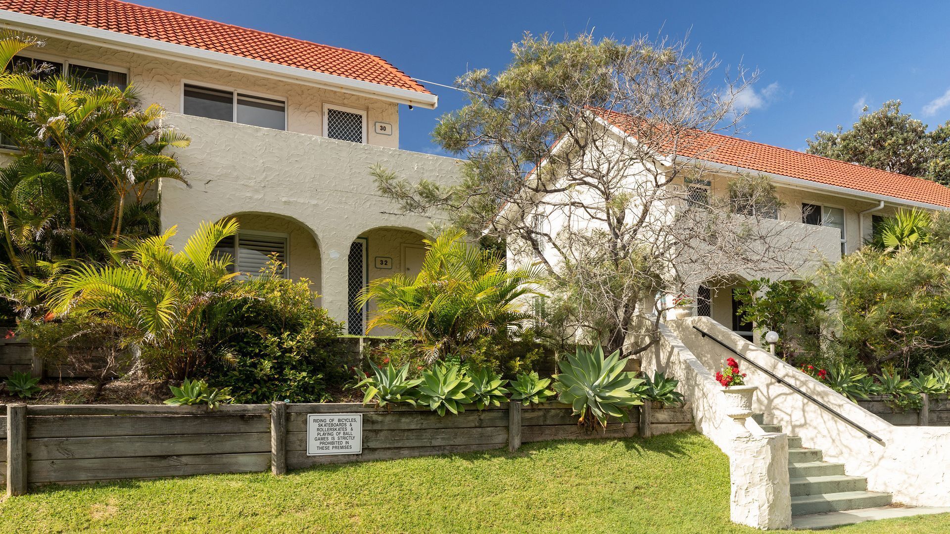 A two-story building with a red-tiled roof, arched windows, and a staircase leading to the entrance.