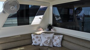 A boat's interior with a cushioned seating area, a fan, and a potted plant. - TRAVEL THE KEYS OR JUST RELAX AT THE DOCK (Key West)