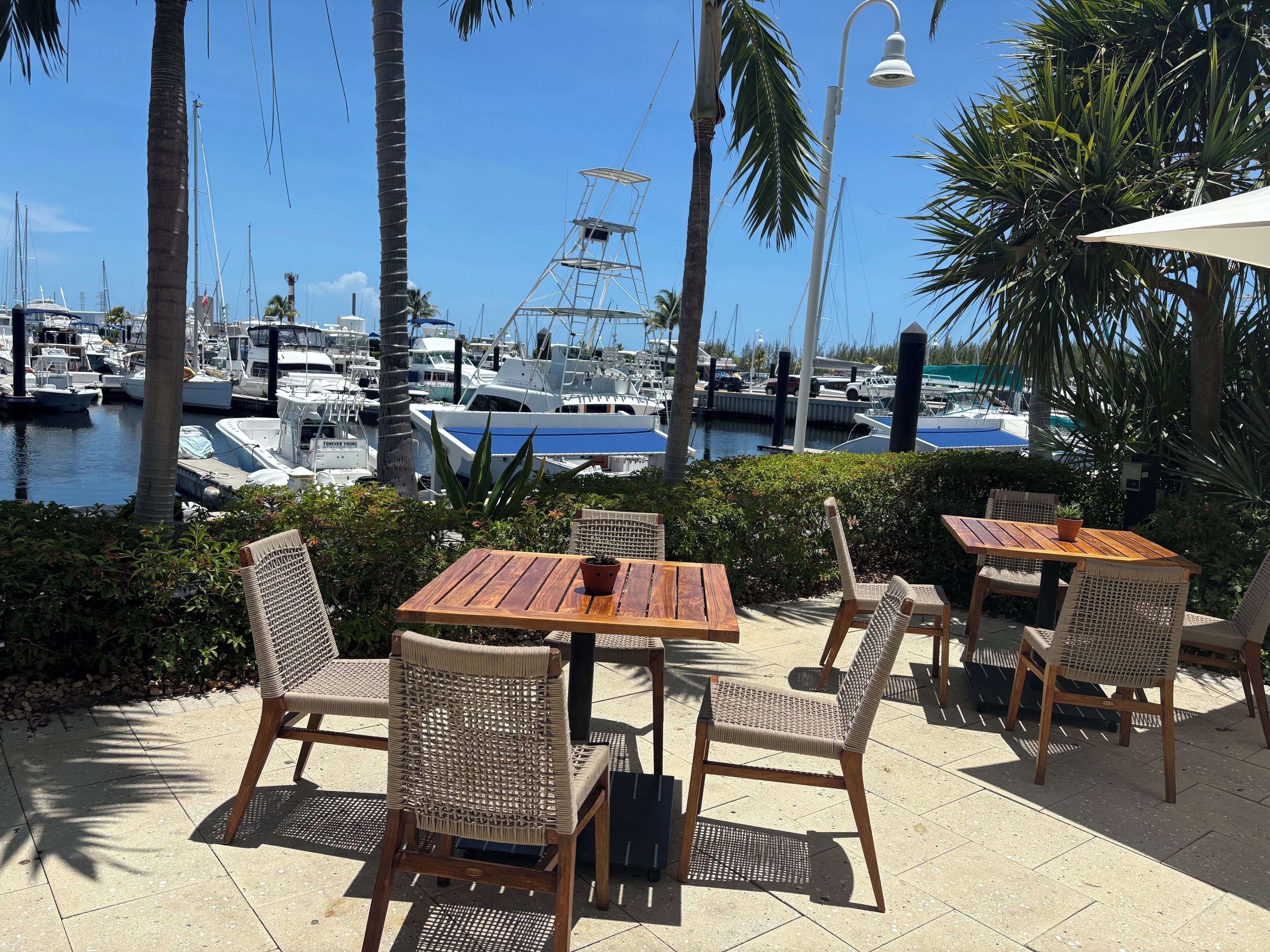 An outdoor seating area with tables and chairs, overlooking a marina with boats.
