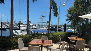 A patio with wooden tables and wicker chairs, overlooking a marina with boats and a clear blue sky. - TRAVEL THE KEYS OR JUST RELAX AT THE DOCK (Key West)