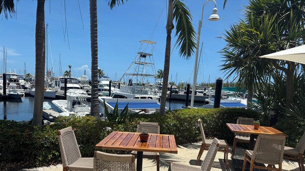 A patio with wooden tables and wicker chairs, overlooking a marina with boats and a clear blue sky. - TRAVEL THE KEYS OR JUST RELAX AT THE DOCK (Key West)