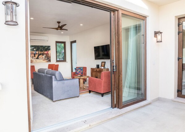 A spacious living area with a gray sofa, a red armchair, and a wooden coffee table. A flat-screen TV is mounted on the wall, and there is a ceiling fan.