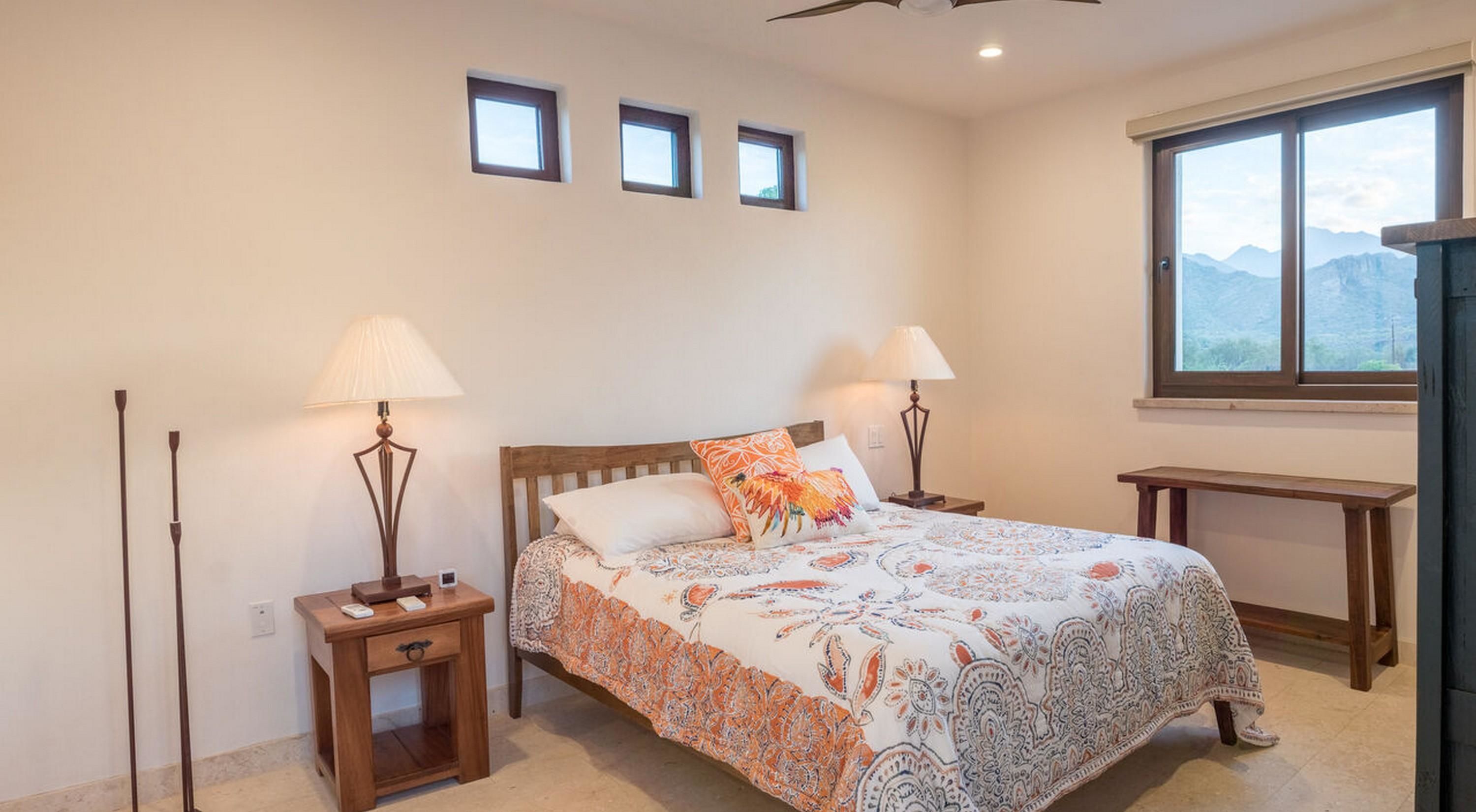 A bedroom with a bed, two bedside tables with lamps, a desk, and a window with a mountain view.