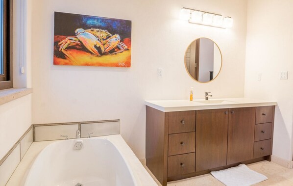 A modern bathroom with a large bathtub, a wooden vanity with a mirror, and a colorful painting on the wall. - Casa Del Gallo 2 BR by Casago (Loreto)