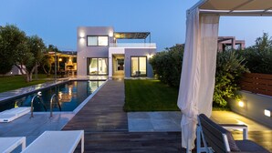 A modern house with a swimming pool, a covered patio, and a well-maintained lawn. - Modern Villa with Unique Architecture & Captivating Sunsets (Skouloufia)