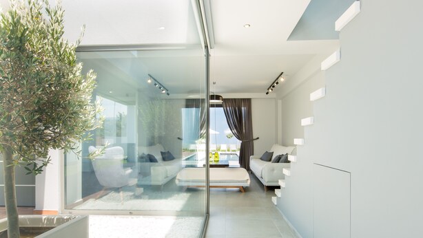 A modern living room with a glass partition, a sofa, a coffee table, and a potted plant. - Modern Villa with Unique Architecture & Captivating Sunsets (Skouloufia)