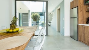 A modern kitchen with a wooden dining table, a stainless steel refrigerator, and a view of the outdoor area. - Modern Villa with Unique Architecture & Captivating Sunsets (Skouloufia)