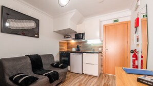 Un espacio habitable compacto con kitchenette, un sofá, una mesita y un extintor.