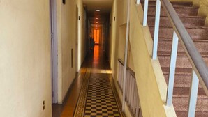 Um corredor com piso xadrez, uma escada à direita e portas à esquerda.