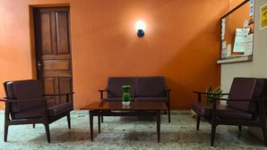 Um quarto com porta de madeira, um sofá, duas poltronas, uma mesa de centro e um pequeno vaso de planta.