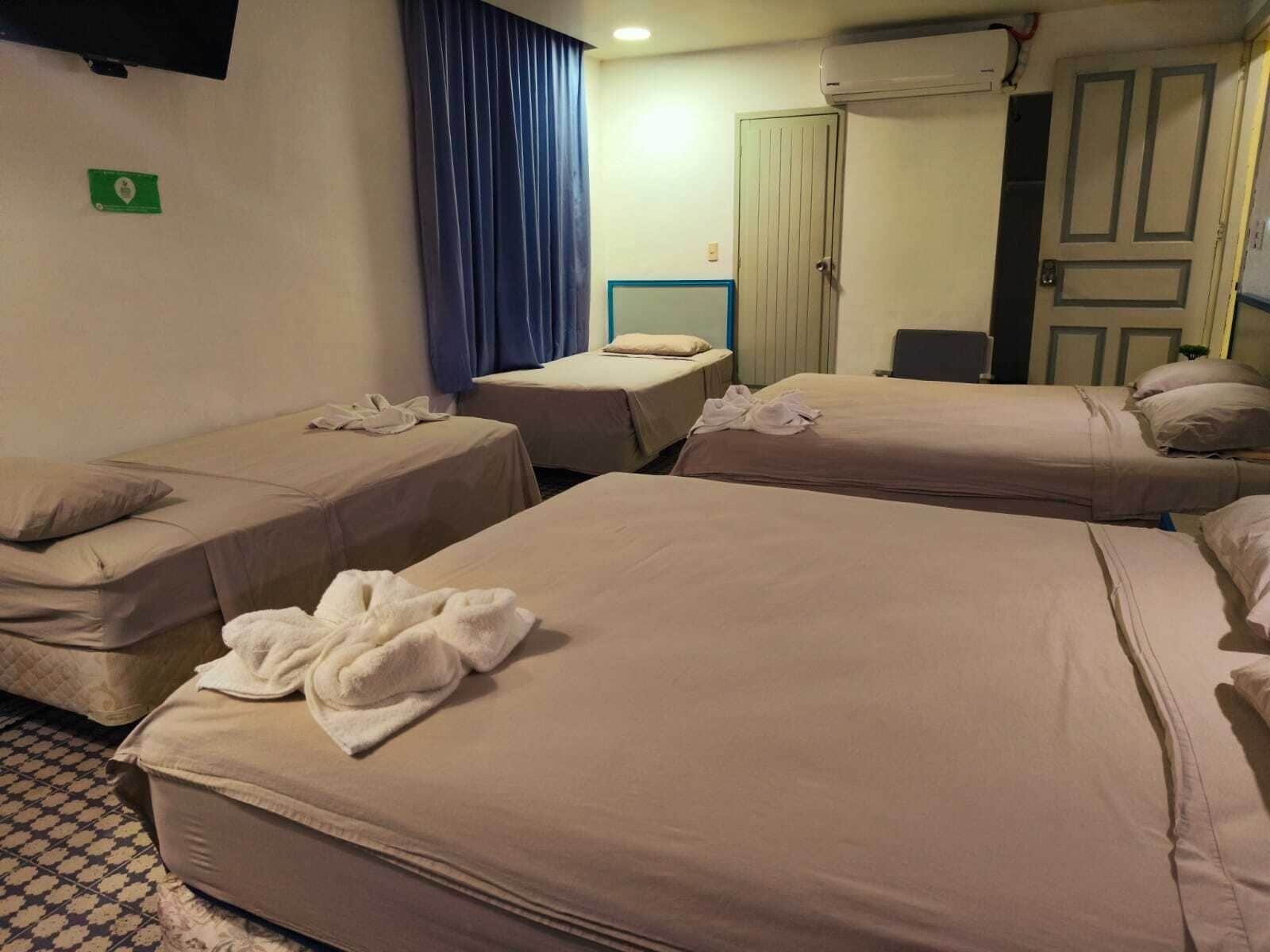 Ein Hotelzimmer mit vier Betten, einem Fernseher, einem Kleiderschrank und einem blauen Vorhang.