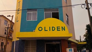 Um hotel chamado "OLIDEN", com fachada azul e amarela marcante, várias janelas e entrada visível.