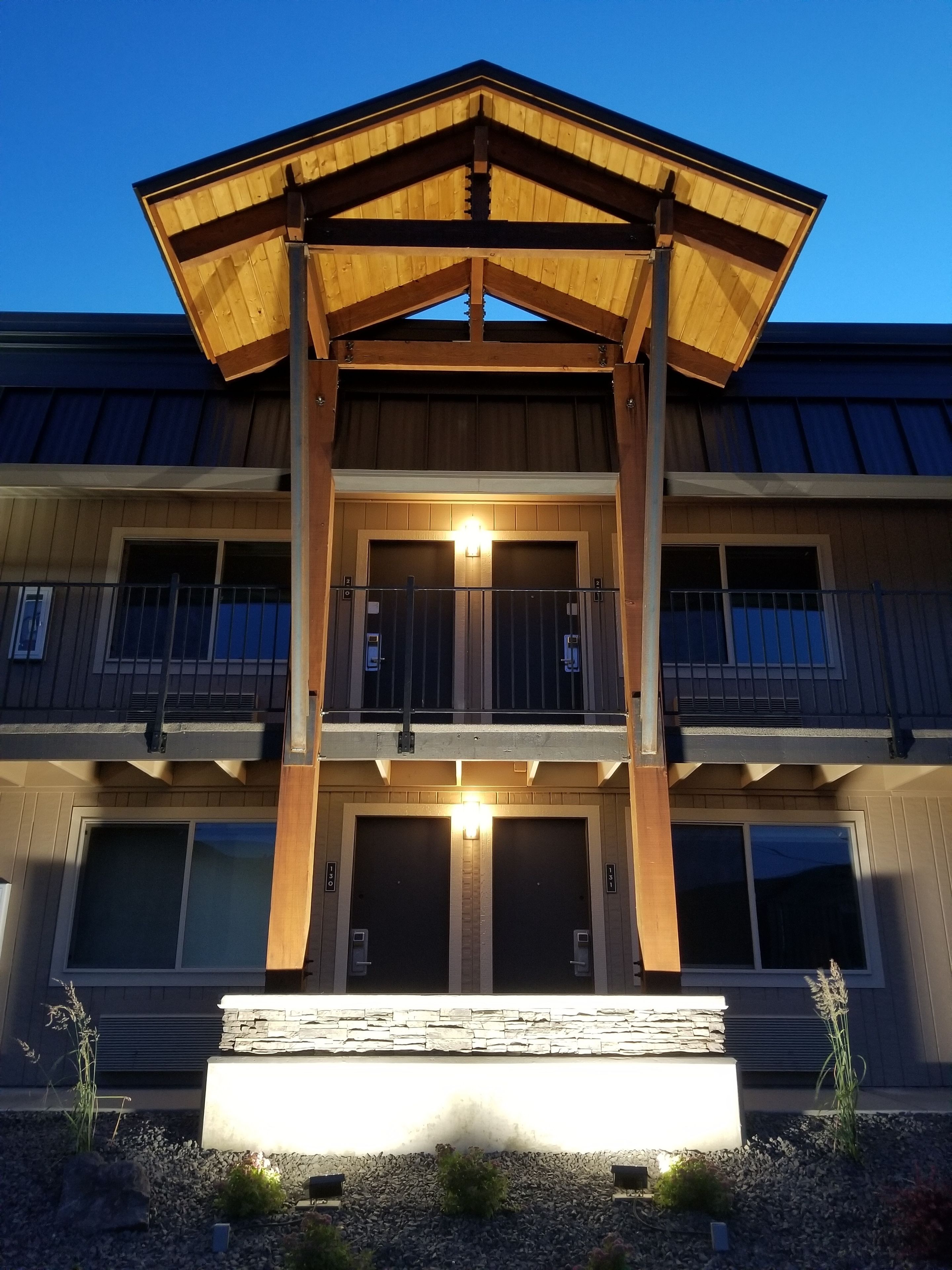 Un edificio de varios pisos con una estructura de madera destacada en la entrada, ventanas grandes y una base de piedra.
