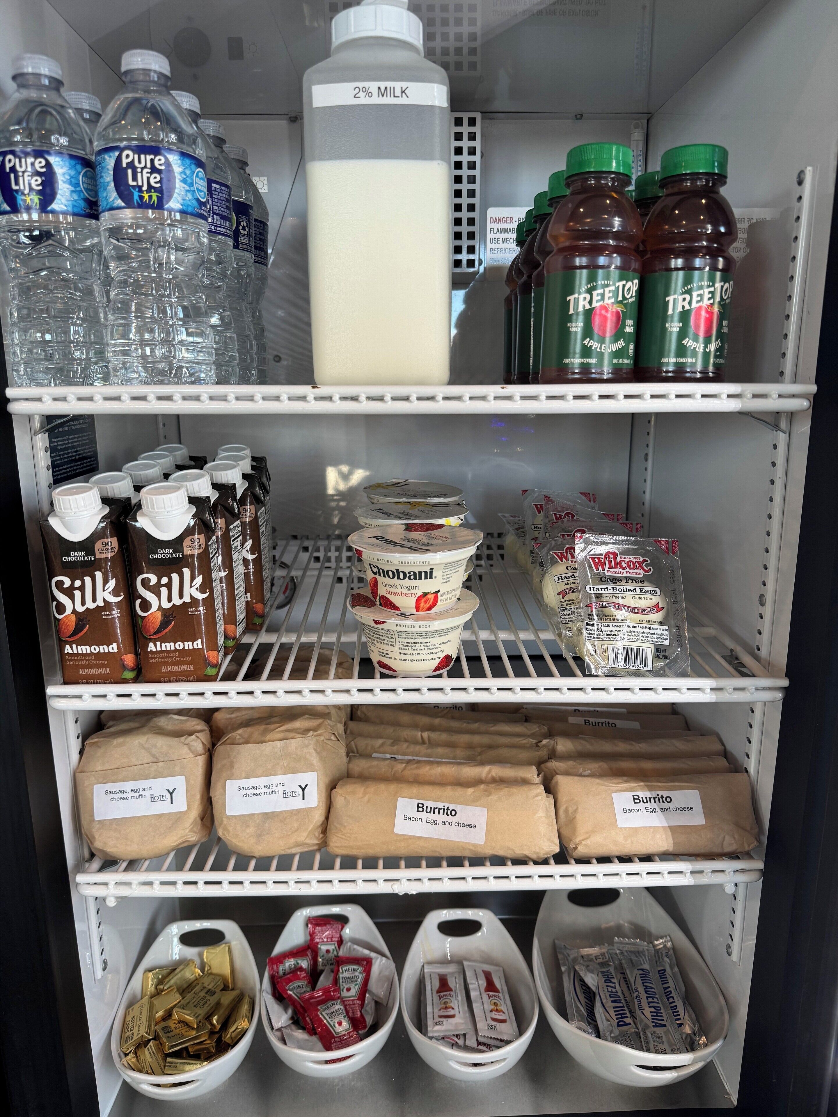Una sección refrigerada con agua embotellada, leche, jugo de manzana, leche de chocolate, yogur y diversos productos para el desayuno.
