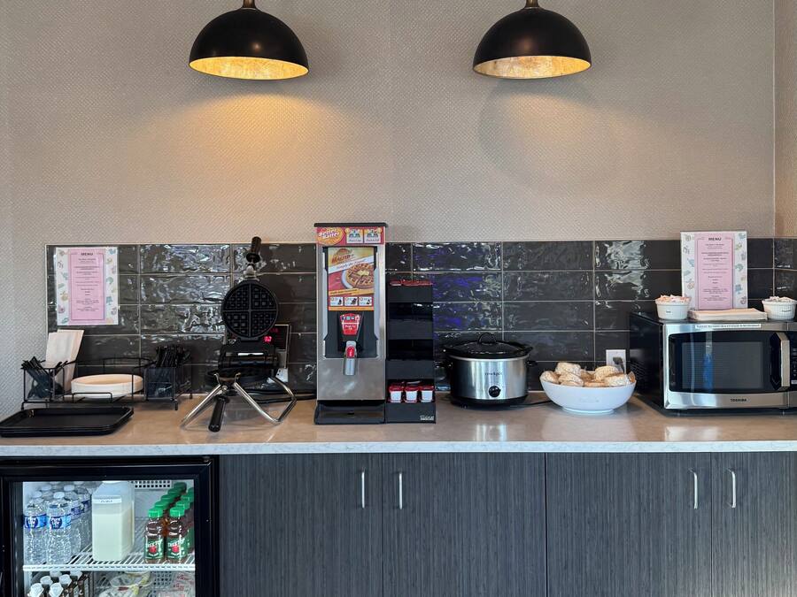 A modern kitchen with a refrigerator, microwave, coffee machine, and a food display.