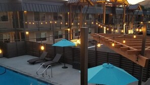 A swimming pool with lounge chairs and umbrellas, surrounded by a wooden deck and a building with balconies. - The Hotel Y, a Dazzler Select by Wyndham (Yakima)