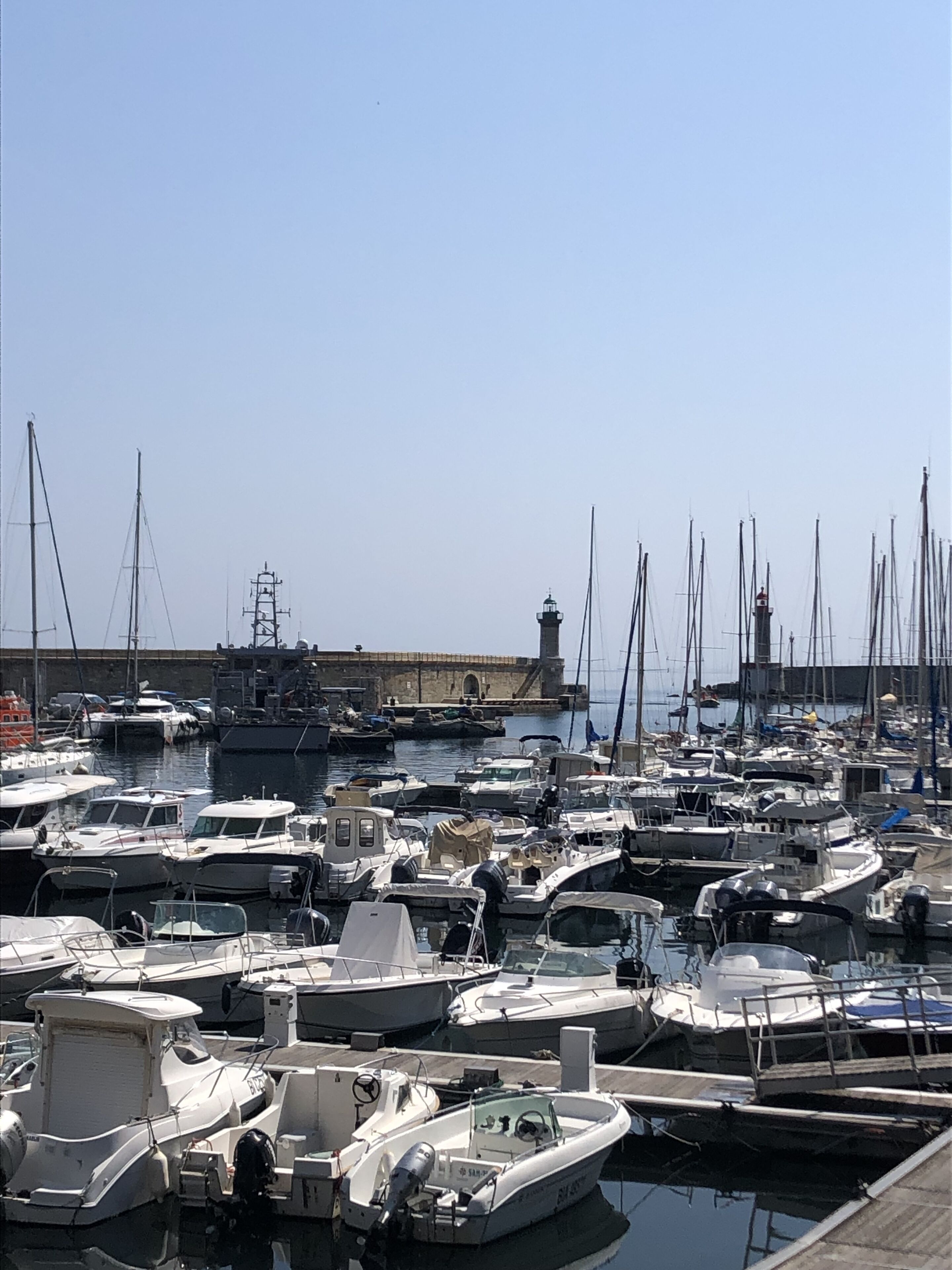 A marina with various boats docked, a lighthouse in the background, and a clear sky.