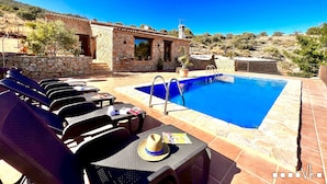 A poolside area with lounge chairs, a table with a hat and magazine, and a stone building with a window overlooking the pool. - Villa CALIMA in Benissa – 3 bedrooms, private pool, sea and mountain views, Wi-Fi and private parking (Benissa)