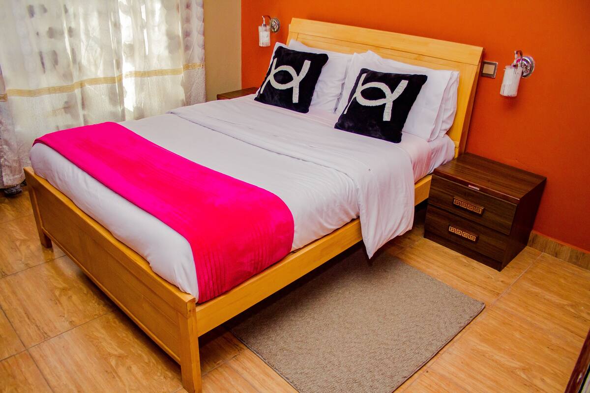 A bed with a wooden frame, white bedding, and two black pillows with the word "Joy".