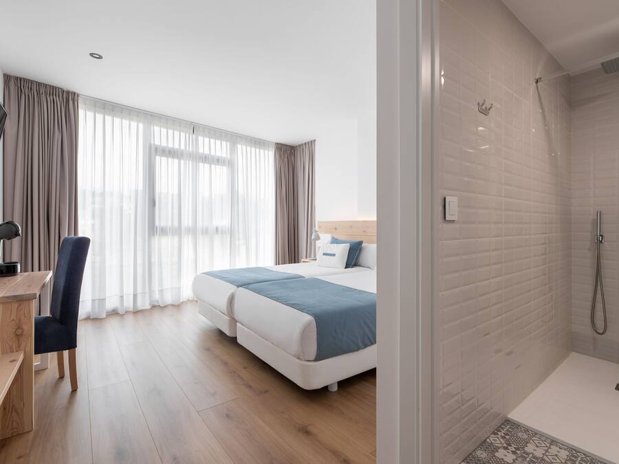 A hotel room with a bed, a desk, a chair, a TV, and a shower area.