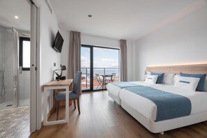 Habitación de hotel con cama, escritorio, silla y un gran ventanal con vista al mar.