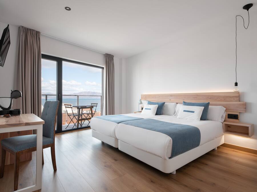 Habitación de hotel moderna con una cama grande, un escritorio y vista al mar.