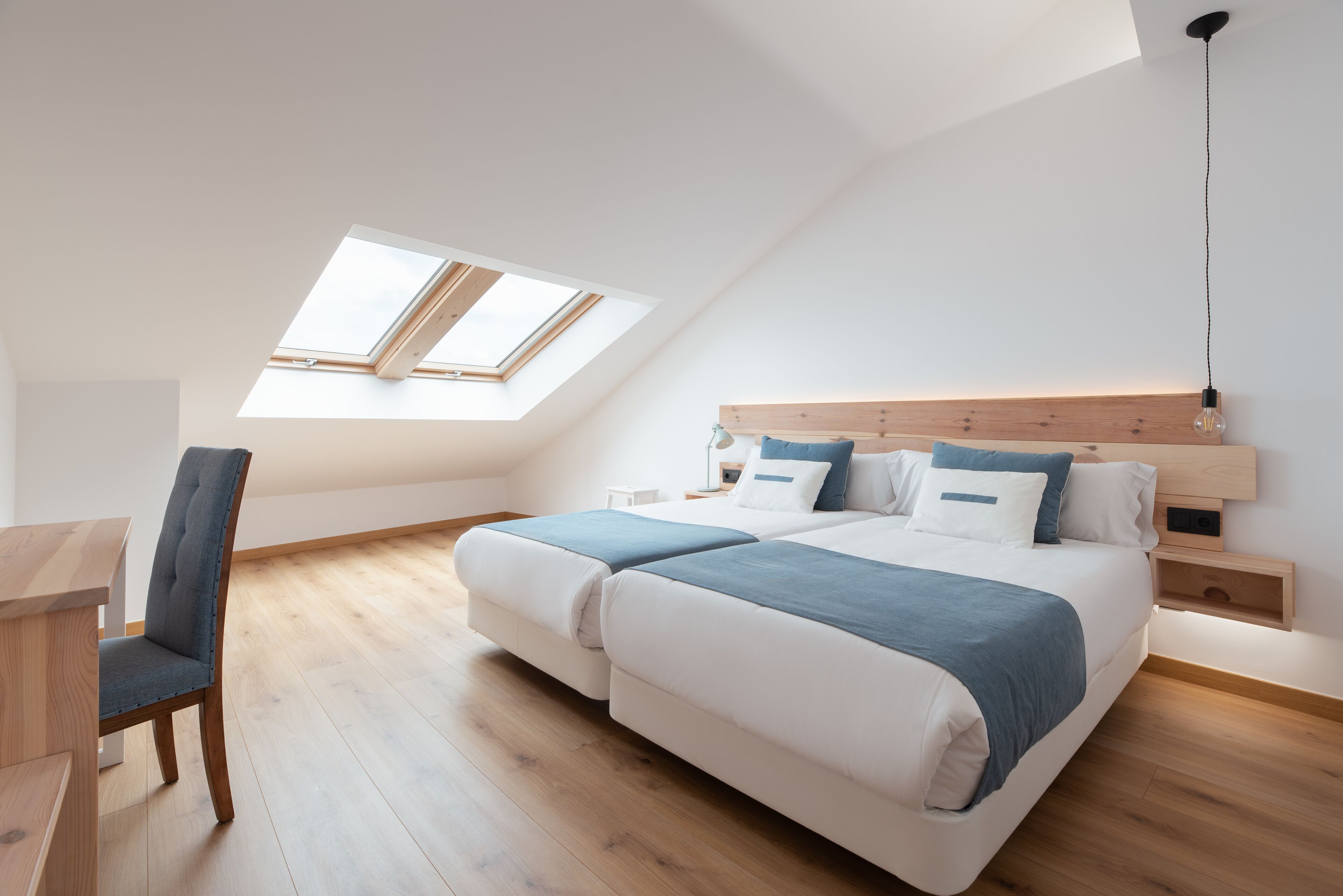 A modern bedroom with a skylight, a bed with a wooden headboard, and a desk with a chair.