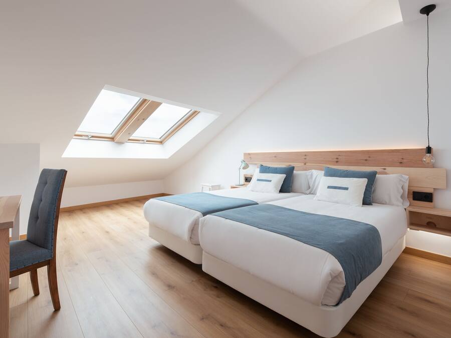 A modern bedroom with a skylight, a bed with a wooden headboard, and a desk with a chair.