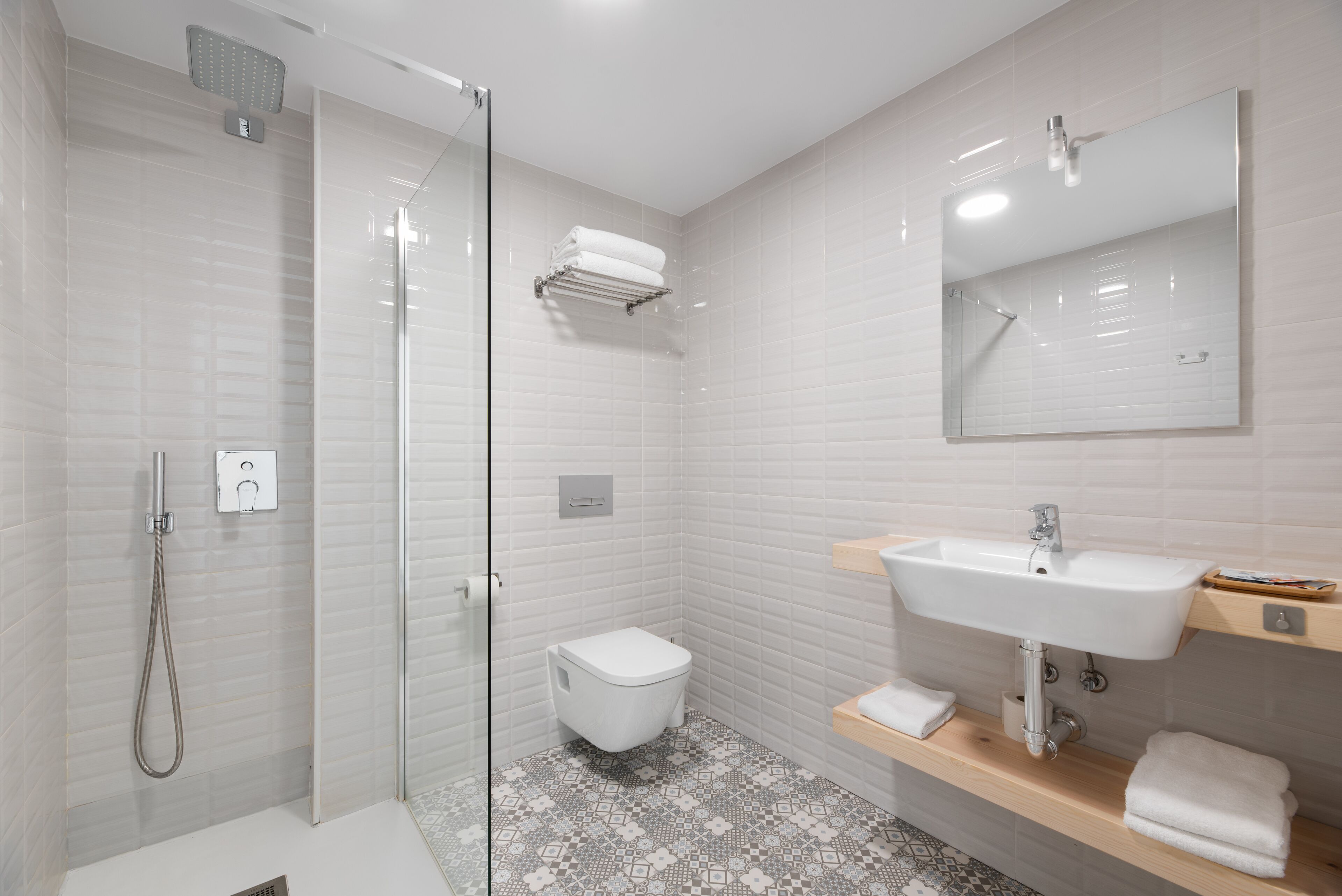 A modern bathroom with a glass-enclosed shower, a white toilet, a sink with a mirror, and a patterned floor.
