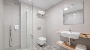 Un bagno moderno con doccia vetrata, un water bianco, un lavandino con specchio e un pavimento decorato.