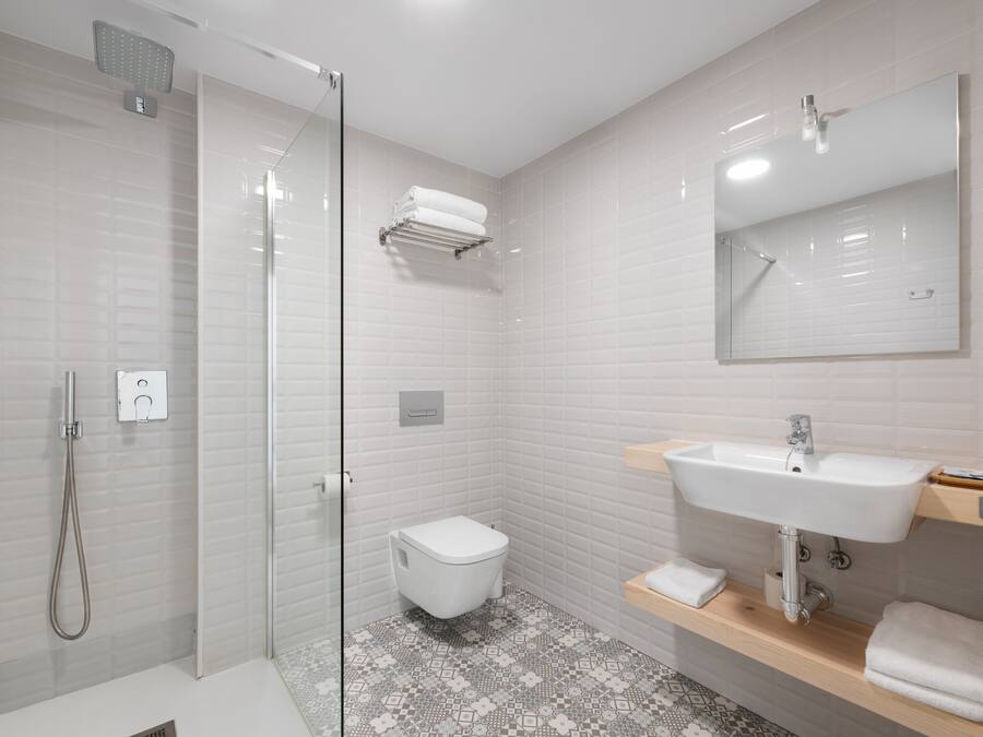 Un bagno moderno con doccia vetrata, un water bianco, un lavandino con specchio e un pavimento decorato.