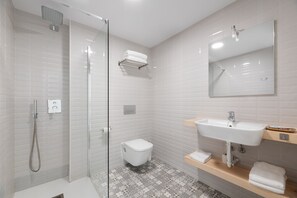 Un baño moderno con ducha de vidrio, inodoro blanco, lavamanos con espejo y suelo estampado.