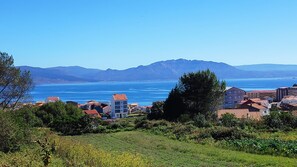 Un pueblo costero con edificios a lo largo del paseo marítimo, un mar azul cristalino y montañas al fondo.