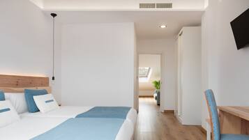 A modern hotel room with two beds, a wooden headboard, a desk with a chair, and a TV on the wall.