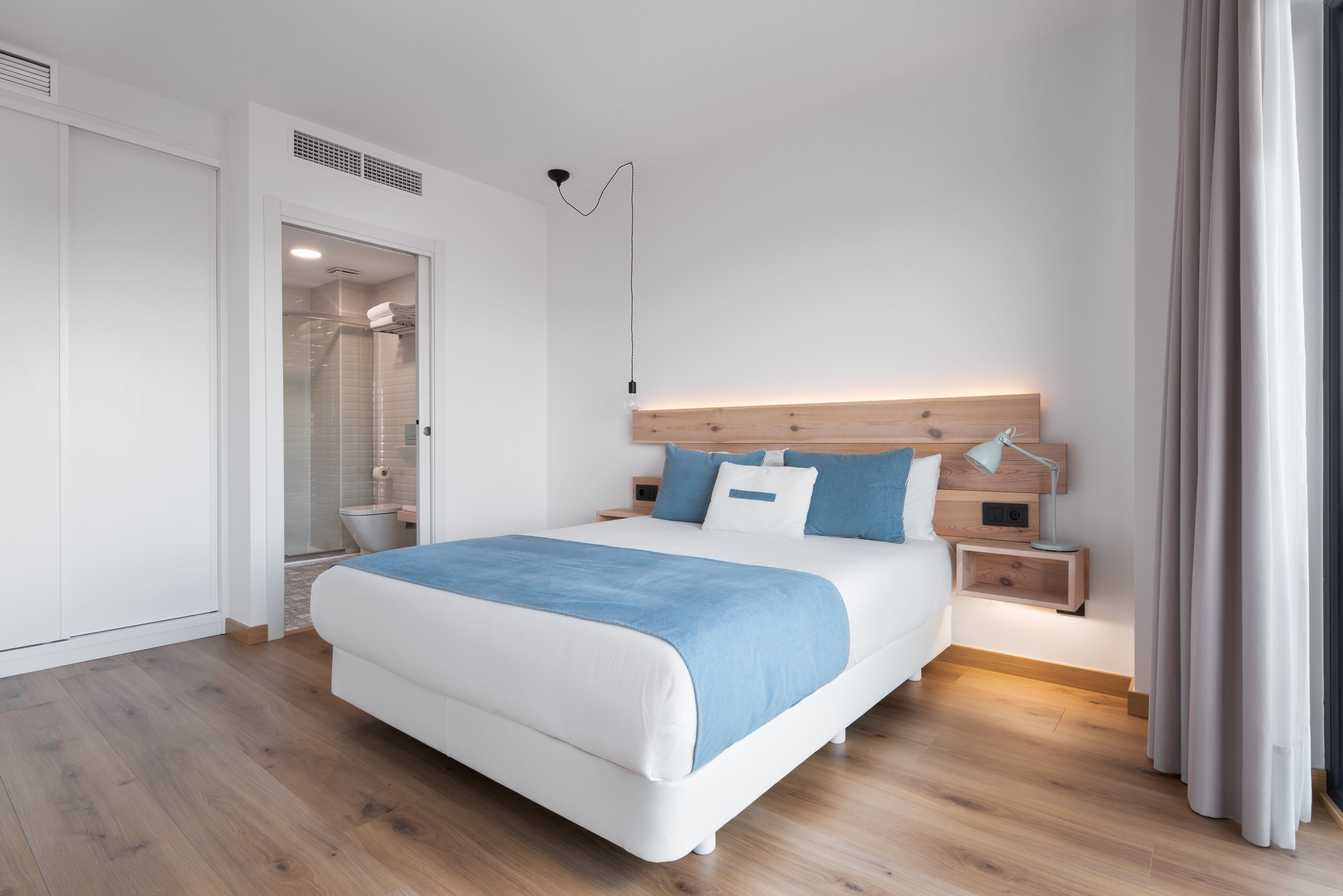 Un dormitorio moderno con una cama grande, cabecera de madera, mesitas de noche y ducha a ras de suelo.