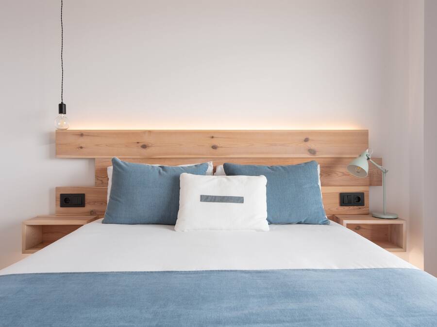 A modern bedroom with a wooden headboard, a white bedspread, and two nightstands with a lamp and a power outlet.