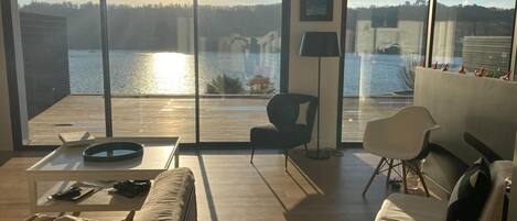 A modern living room with a large sliding glass door leading to a deck overlooking a body of water.