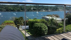 Un balcón con vista a un puerto, barcos y una ladera boscosa.