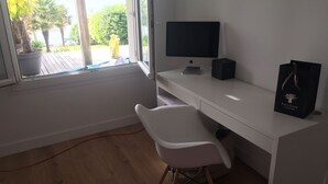 Un espacio de oficina moderno con un escritorio, una silla y un monitor de computadora. Hay una ventana con vista a áreas verdes y un edificio.