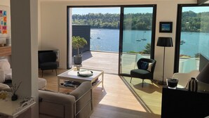 Una sala de estar moderna con un amplio ventanal corredera que da a un balcón con vistas a un lago con barcos.