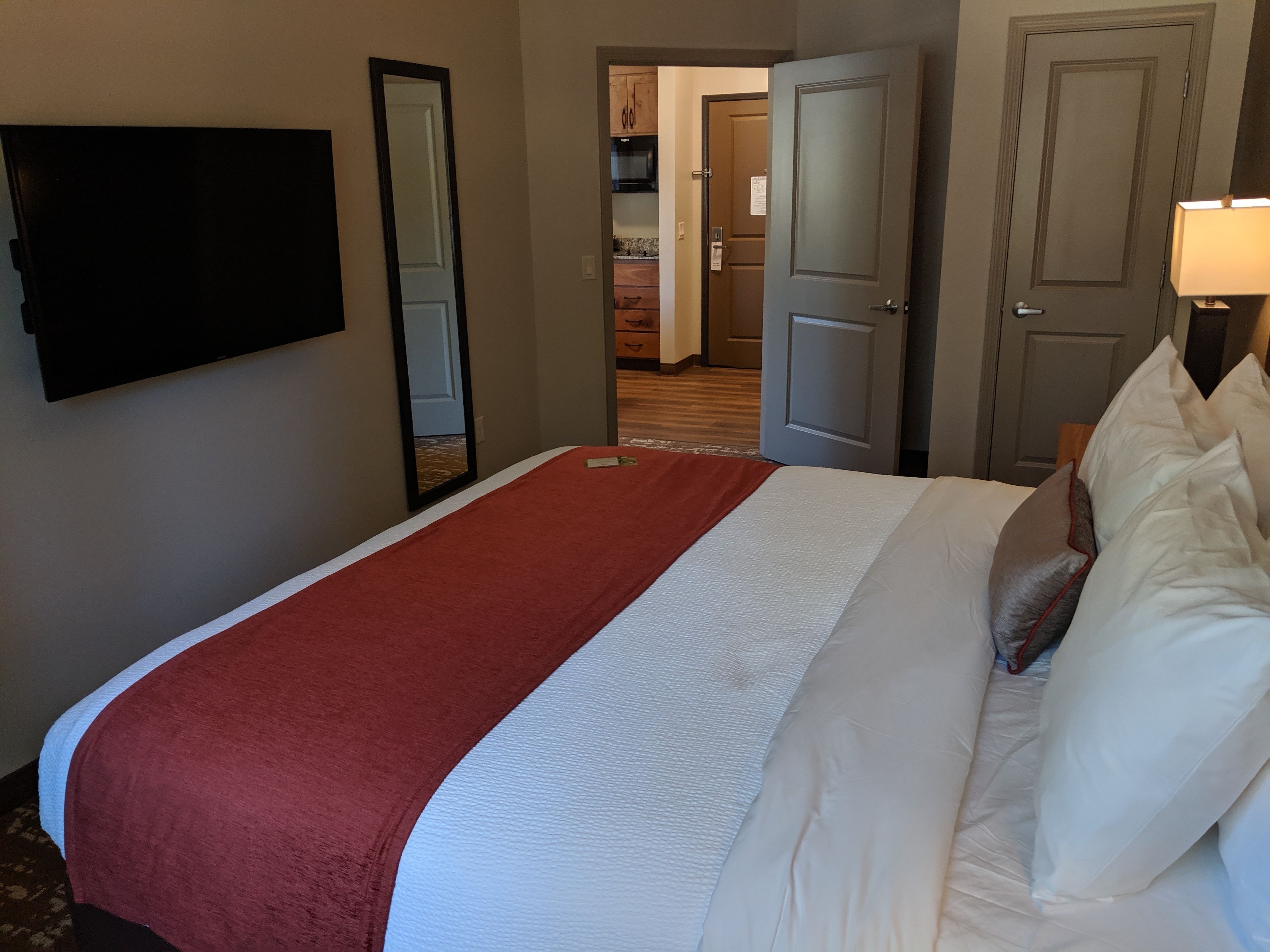 A hotel room with a large bed, a flat-screen TV mounted on the wall, and a door leading to a bathroom.