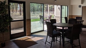 A spacious indoor patio with wicker furniture, a clock on the wall, and a view of a fenced outdoor area. - GrandStay Hotel & Suites (Sisters)