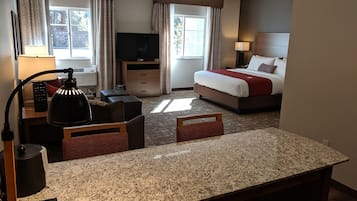 Habitación de hotel con cama, escritorio, silla, televisor, lámpara y ventana con cortinas.