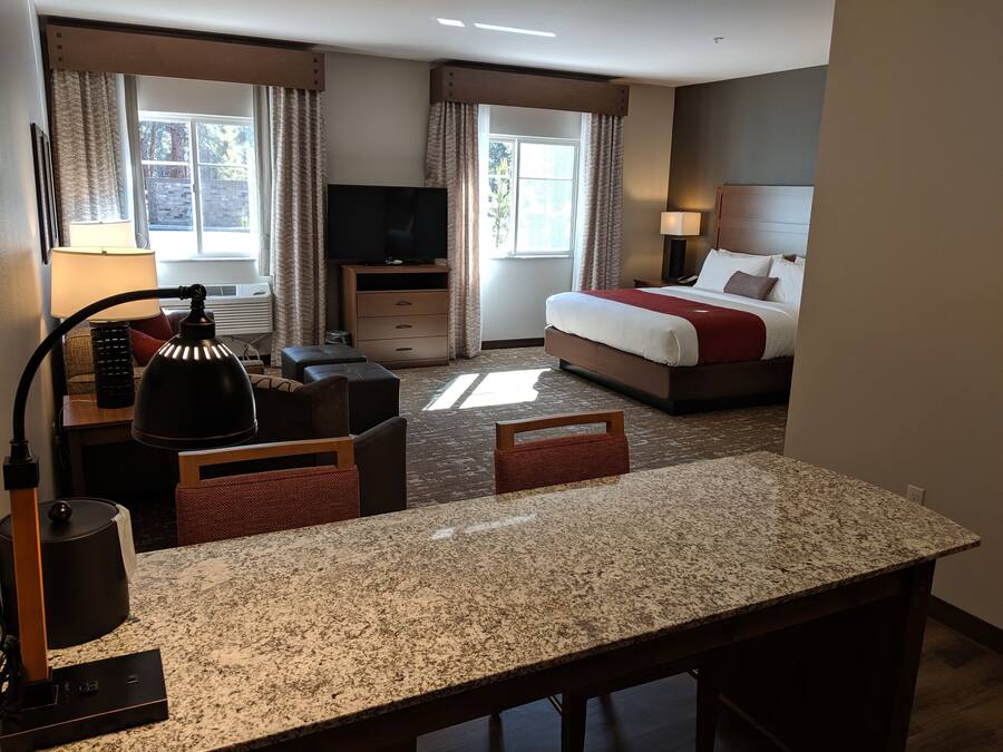 Habitación de hotel con cama, escritorio, silla, televisor, lámpara y ventana con cortinas.